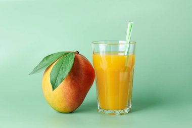 Bardakta lezzetli mango suyu ve yeşil arka planda taze meyve.