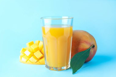 Bardakta lezzetli mango suyu ve açık mavi arka planda taze meyve, yakın plan.