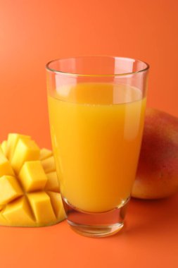 Bardakta lezzetli mango suyu ve turuncu arka planda taze meyve, yakın plan.