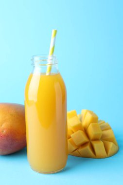 Cam şişede lezzetli mango suyu ve açık mavi arka planda taze meyve.