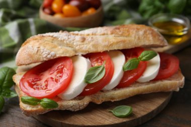 Mozarella peynirli, domatesli ve ahşap masadaki fesleğenli lezzetli sandviç.