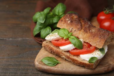 Mozarella peynirli, domatesli ve ahşap masadaki fesleğenli lezzetli sandviç, yakın plan. Metin için boşluk