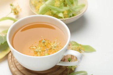 Fincanda taze ıhlamur çayı ve beyaz masada çiçekler, yakın plan.