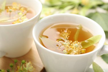 Fincanlarda taze ıhlamur çayı ve beyaz masada çiçekler, yakın plan.