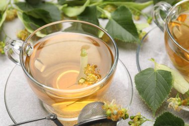 Fincanlarda taze ıhlamur çayı ve açık gri masada çiçekler, yakın plan.