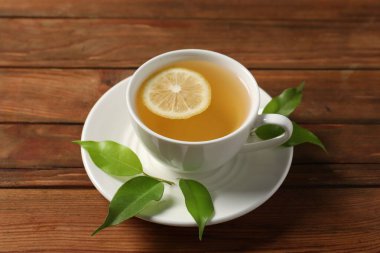 Lezzetli yeşil çay, fincanda limon ve ahşap masa üzerinde yapraklar.