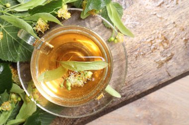 Fincanda nefis ıhlamur çayı, ahşap masada yapraklar ve çiçekler, üst manzara.