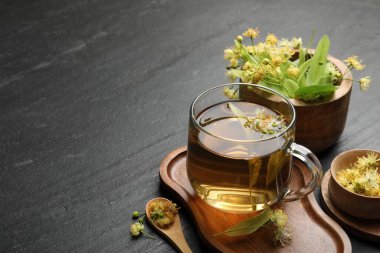 Lezzetli ıhlamur çayı fincanda, kaşıkta, yapraklarda ve çiçeklerde koyu dokulu masada, yakın plan. Metin için boşluk