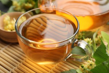 Fincanda lezzetli ıhlamur çayı, bambu hasırında yapraklar ve çiçekler, yakın plan.