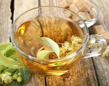 Lezzetli ıhlamur çayı, şeker küpleri, yapraklar ve çiçekler ahşap masada, yakın plan.