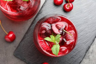 Buzlu vişneli gazoz, böğürtlen ve nane şekeri gri masada, düz yerde.