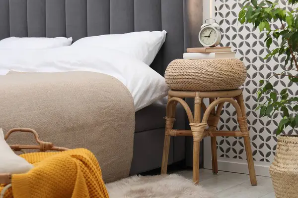 Çalar saati olan yan masa ve yatağın yanında kitaplar.