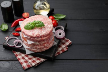 Hamburger için taze çiğ köfte, siyah ahşap masada baharatlar ve domatesler, yakın plan. Metin için boşluk
