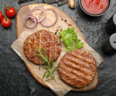 Lezzetli hamburger köfteleri, domatesler ve baharatlar siyah masada, düz yerde