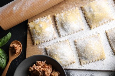 Pişmemiş ravioli, merdane, bolonez ve fesleğen siyah masada, düz yatıyordu.