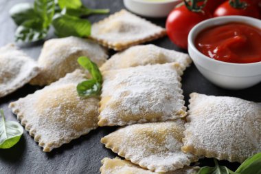 Pişmemiş ravioli, sos, domates ve fesleğen siyah masada, yakın plan.