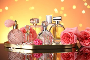 Farklı parfüm şişeleri ve çiçekler ayna yüzeyinde turuncu arka planda bulanık ışıklarla, yakın plan