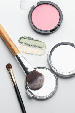Beyaz arka planda farklı makyaj ürünleri ve fırçalar, düz konum