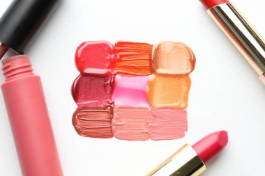Beyaz arka planda renkli dudak parlatıcıları ve rujlar, düz bir zemin.