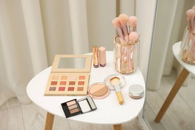 Farklı makyaj ürünleri ve fırçalar aynanın yanındaki beyaz masada.