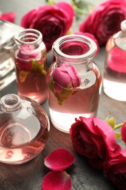 Gri desenli masa üzerinde aromatik esanslı yağlar ve güllerle parfüm şişelerini aç, yakın plan.