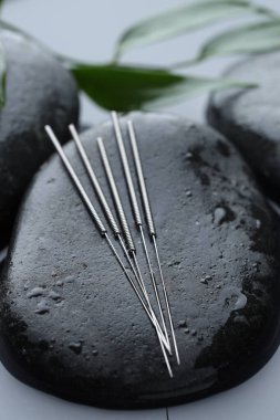 Akupunktur iğneleri, ıslak spa taşları ve su yüzeyinde yapraklar, yakın çekim.