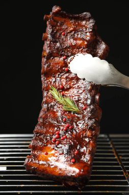 Siyah arka planda ızgaradan maşayla leziz domuz pirzolası alıp yakın plan çekiyoruz.