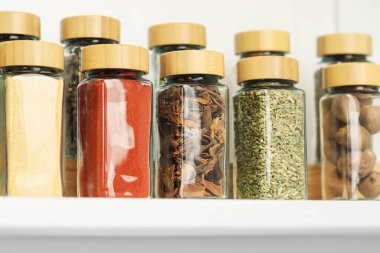 Beyaz masadaki kavanozlardaki farklı aromatik baharatlar, yakın plan.