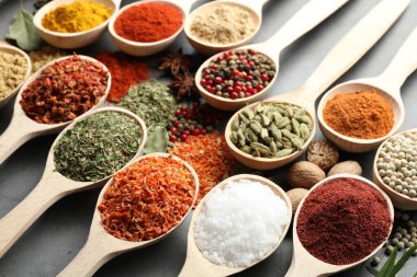 Gri masadaki kaşıklardaki farklı baharatlar, yakın plan.