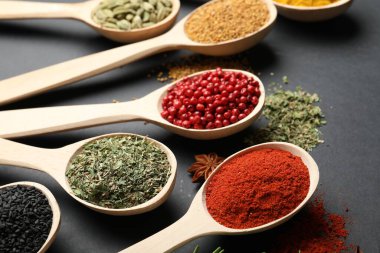 Siyah masada kaşıklardaki farklı aromatik baharatlar, yakın plan.