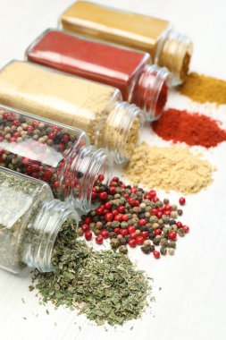 Beyaz masadaki kavanozlarda farklı aromatik baharatlar, yakın plan.