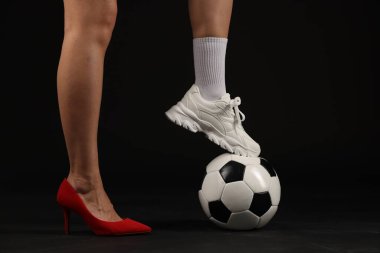 Arka planda futbol topu olan yüksek topuklu ayakkabılı ve spor ayakkabılı bir kadın.