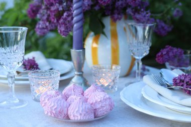 Güzel leylak çiçekleri, zephyrler, tabaklar, çatal bıçaklar, bardaklar ve mumlar bahçede, yakın plan