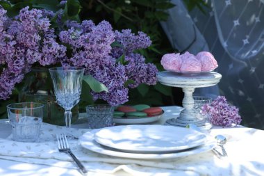 Bahçedeki masada güzel leylak çiçekleri, tatlılar, tabaklar, bardaklar ve çatal bıçaklar.