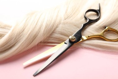 Açık pembe arka planda saç teli ve makas, yakın plan.