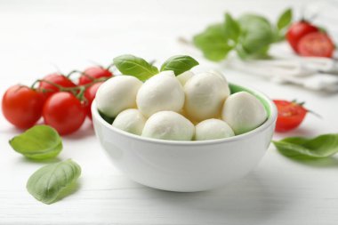 Lezzetli mozzarella peynir topları kasede fesleğen ve domatesler beyaz ahşap masada, yakın plan.