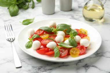 Beyaz mermer masada servis edilen mozarellalı, domatesli ve fesleğenli lezzetli salata.