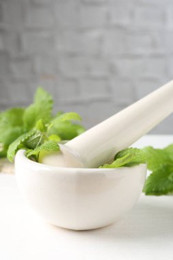 Taze limon merhemi yaprakları ve beyaz ahşap masada havan topuzu, yakın plan.