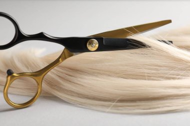 Açık gri arka planda makasla sarı saç tokası kesiliyor. Yakın plan.