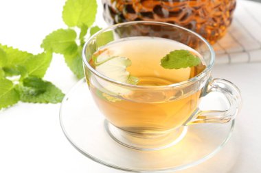 Cam bardakta Aromatik limon merhemi çayı, çaydanlık ve beyaz masada taze yapraklar, yakın plan.
