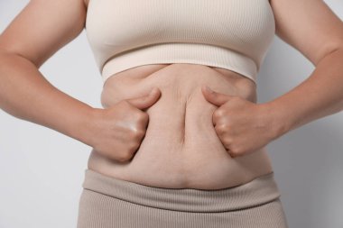 Hafif arka planda aşırı göbek yağı olan kadın, yakın plan. Aşırı kilolu