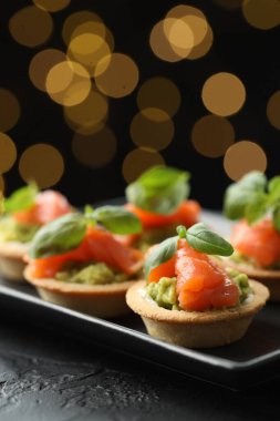 Siyah masadaki lezzetli kanepeler karanlık arka planda bulanık ışıklarla, yakın plan. Bokeh etkisi