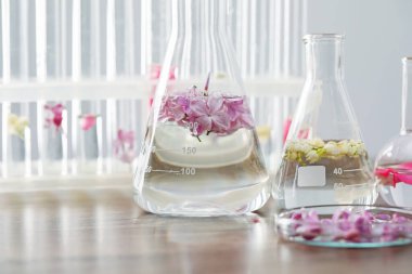 Lüks parfüm yapıyorum. Temel yağlar cam süslemede ve çiçekler açık ahşap masada, yakın plan