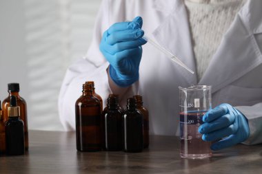 Laboratuardaki ahşap masada lüks parfüm üreten profesyonel parfümcü.