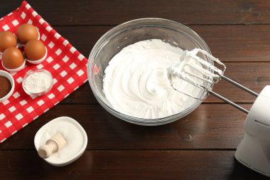 Krem şantili kase, el çırpıcı ve malzemeler ahşap masada, yakın plan.