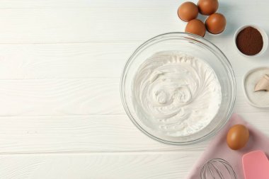 Krem şanti, çırpma ve malzemelerle dolu bir kase beyaz ahşap masa, düz yatak. Metin için boşluk