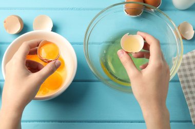 Açık mavi ahşap masada yumurta sarısını beyazdan ayıran kadın.
