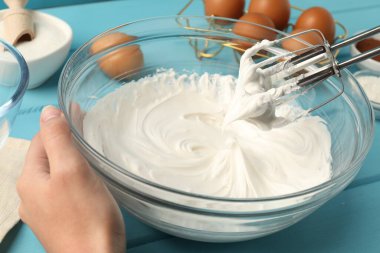 Açık mavi ahşap masada el çırpıcı kremalı bir kadın, yakın plan.