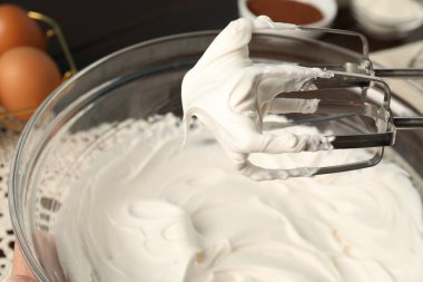 Masada çırpılmış krema ve çırpılmış kremayla el çırpıcı, yakın plan.