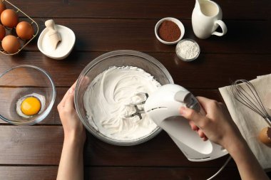Ahşap masada el çırpıcı kremalı bir kadın.